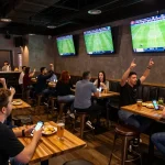 Fans engaging with nowgoal for real-time sports betting in a vibrant sports bar atmosphere